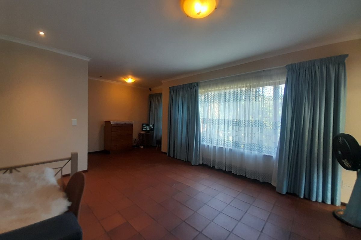 Spacious living room featuring terracotta tile flooring, neutral walls, and a large window with natural light.
