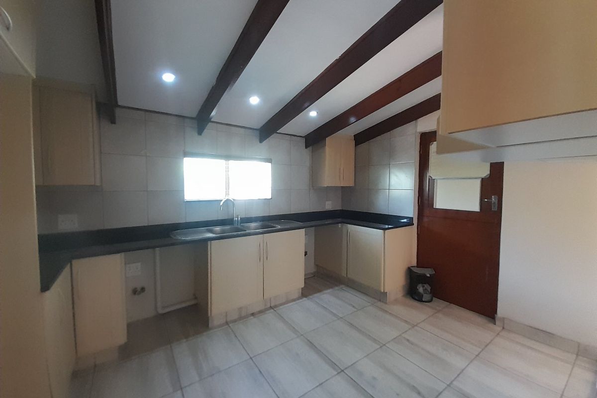 A functional kitchen featuring built-in cabinetry, granite countertops, a double basin sink, and exposed timber ceiling beams with tiled flooring.