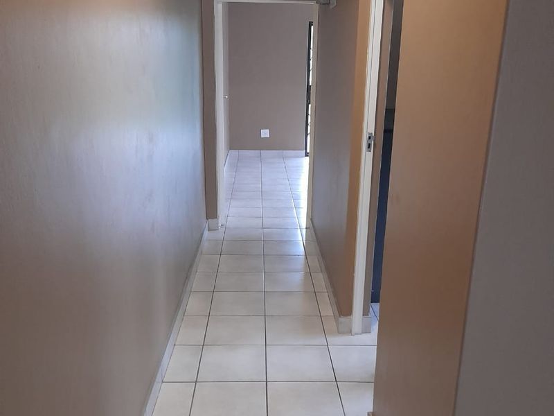 A clean, empty hallway featuring neutral wall paint and light-colored floor tiles, providing a bright transition between living spaces.
