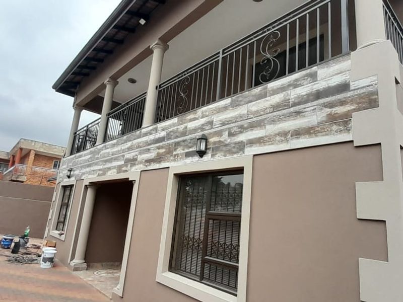 Rear exterior view of the apartment building featuring a balcony with wrought iron railings, decorative stone cladding, and paved ground area.
