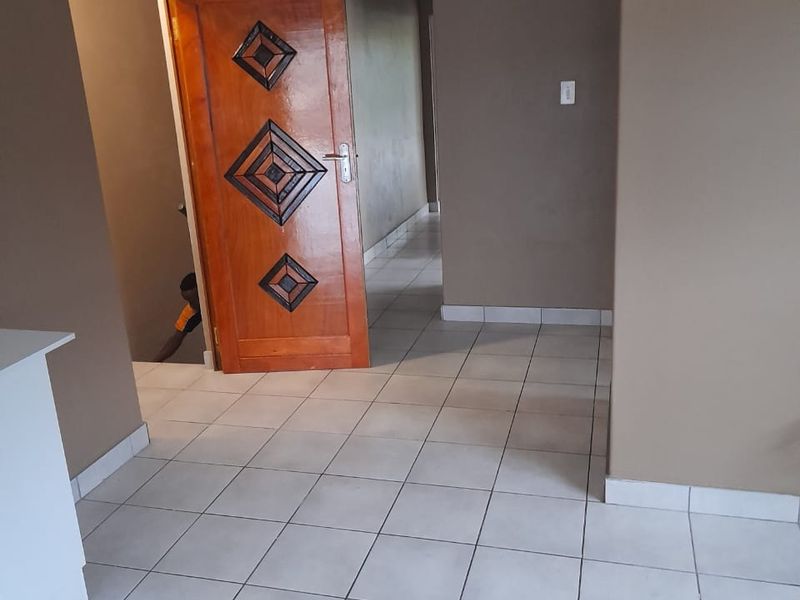A vacant hallway featuring neutral wall paint, tiled flooring, and a decorative wooden door leading to an adjacent room.