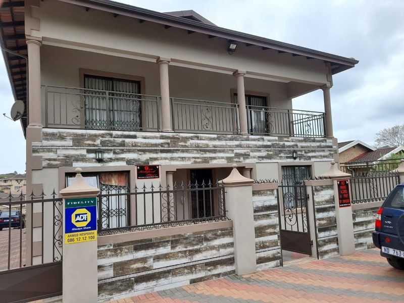 Front elevation of a two-story apartment building featuring a stone-clad facade, wrought iron security fencing, and an upper-level balcony.