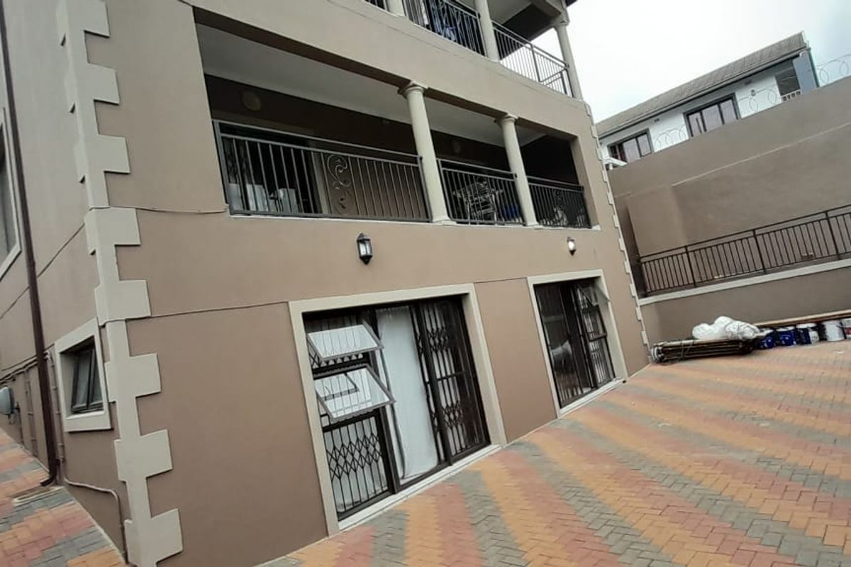 Rear view of the apartment building featuring a paved driveway, multi-level balconies with metal railings, and security gates on the ground floor access points.