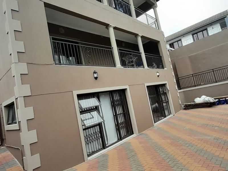Rear view of the apartment building featuring a paved driveway, multi-level balconies with metal railings, and security gates on the ground floor access points.