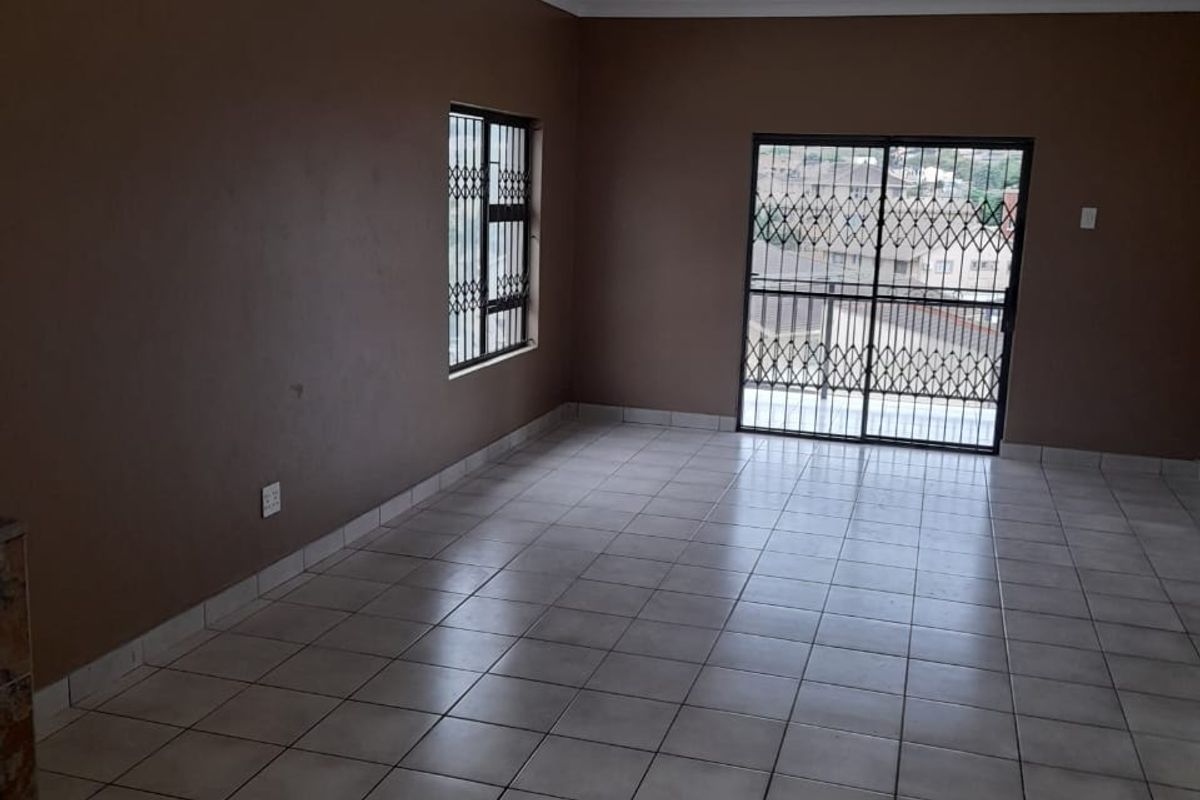 An empty, open-plan living area featuring neutral tiled flooring, a sliding glass door with security gate, and window security bars.