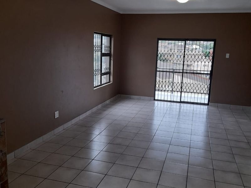 An empty, open-plan living area featuring neutral tiled flooring, a sliding glass door with security gate, and window security bars.
