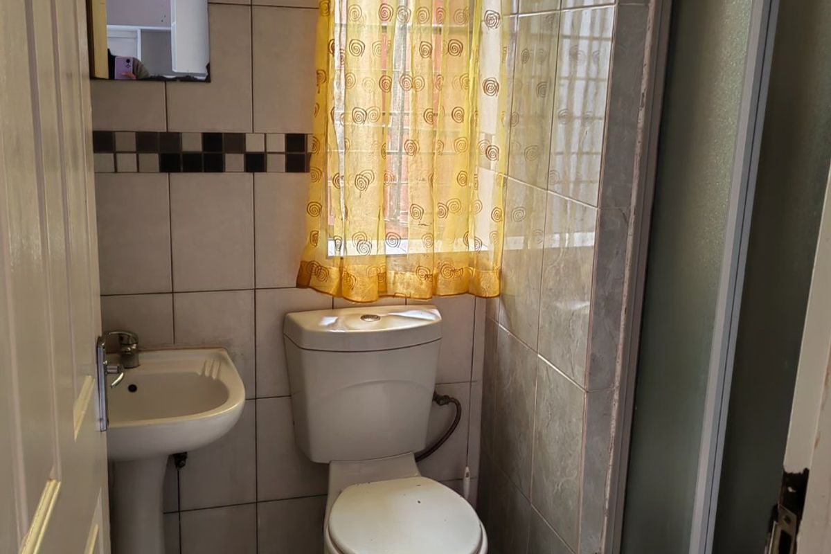 A compact bathroom featuring a pedestal basin, toilet, and shower enclosure with tiled walls and flooring.