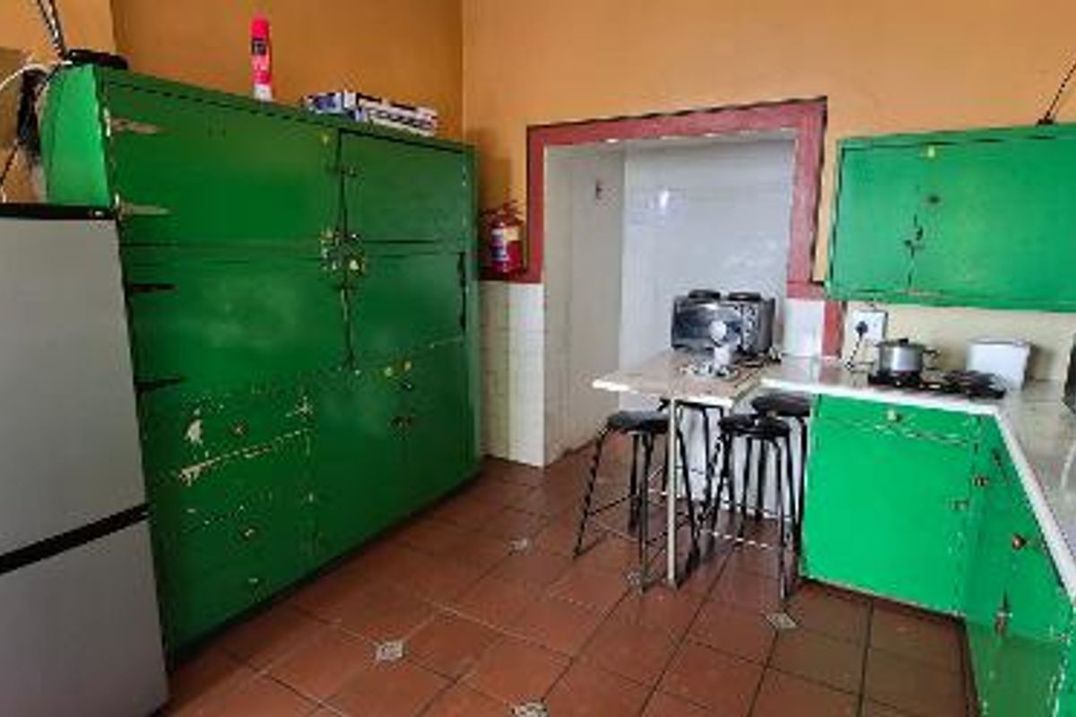 A dated kitchen featuring green built-in cabinetry, tiled flooring, and a tiled splashback, requiring cosmetic updates to improve its overall aesthetic and functionality.