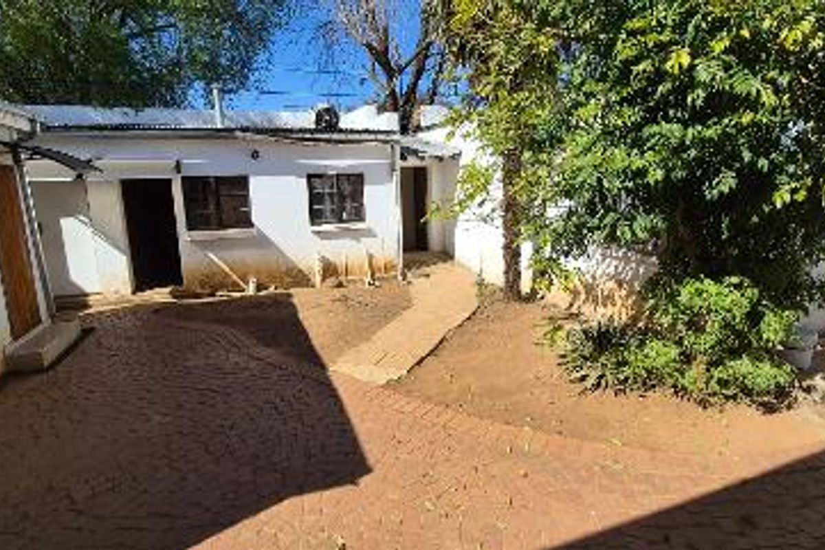 Rear courtyard area featuring paved flooring and access to multiple exterior doors, requiring maintenance to the building facade and paintwork.