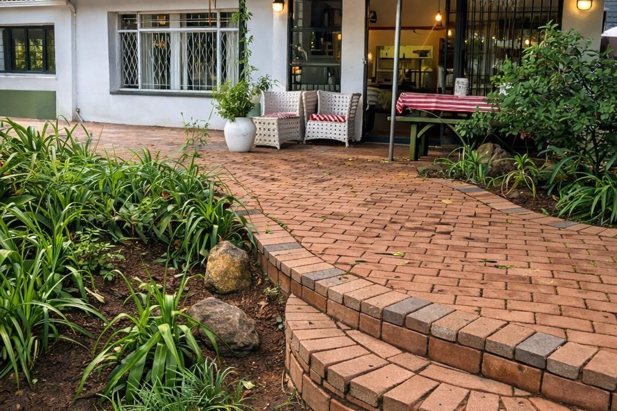 A well-maintained rear exterior featuring a brick-paved patio, tiered brick steps, and sliding glass doors leading into the home.