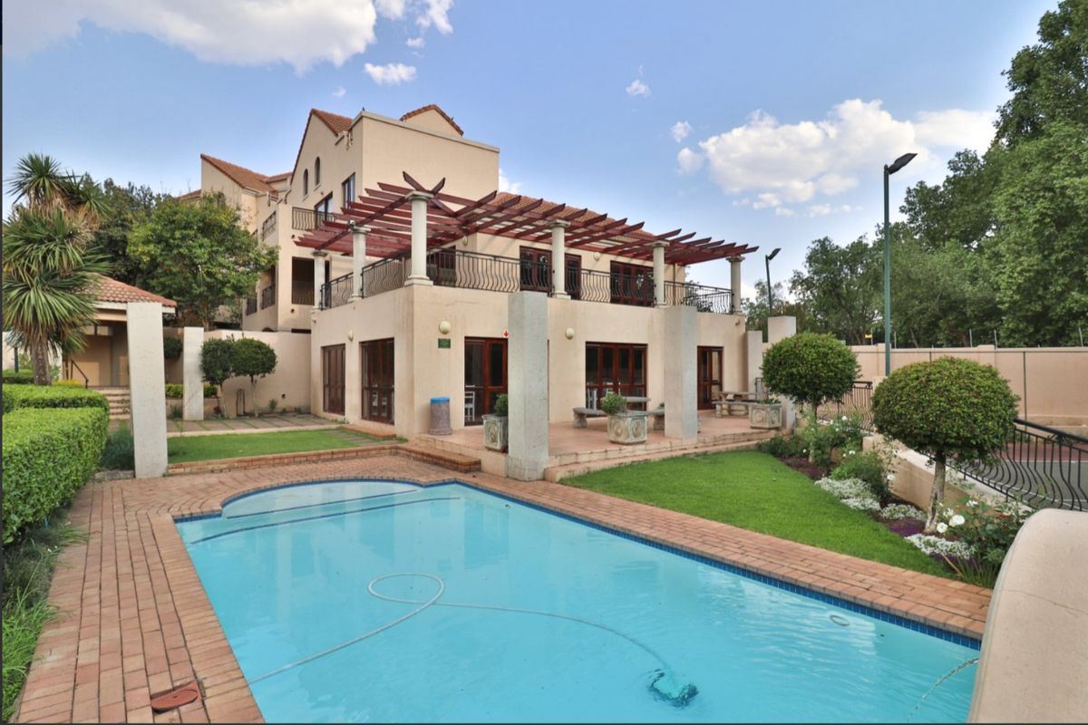 Rear view of the apartment complex featuring a swimming pool, landscaped garden, and a covered patio area with a wooden pergola.