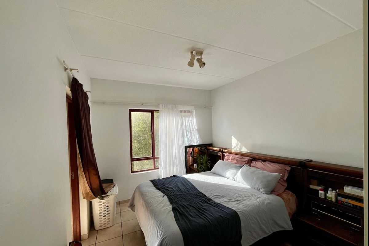 A functional bedroom featuring tiled flooring, a ceiling-mounted spotlight, and a window allowing natural light.
