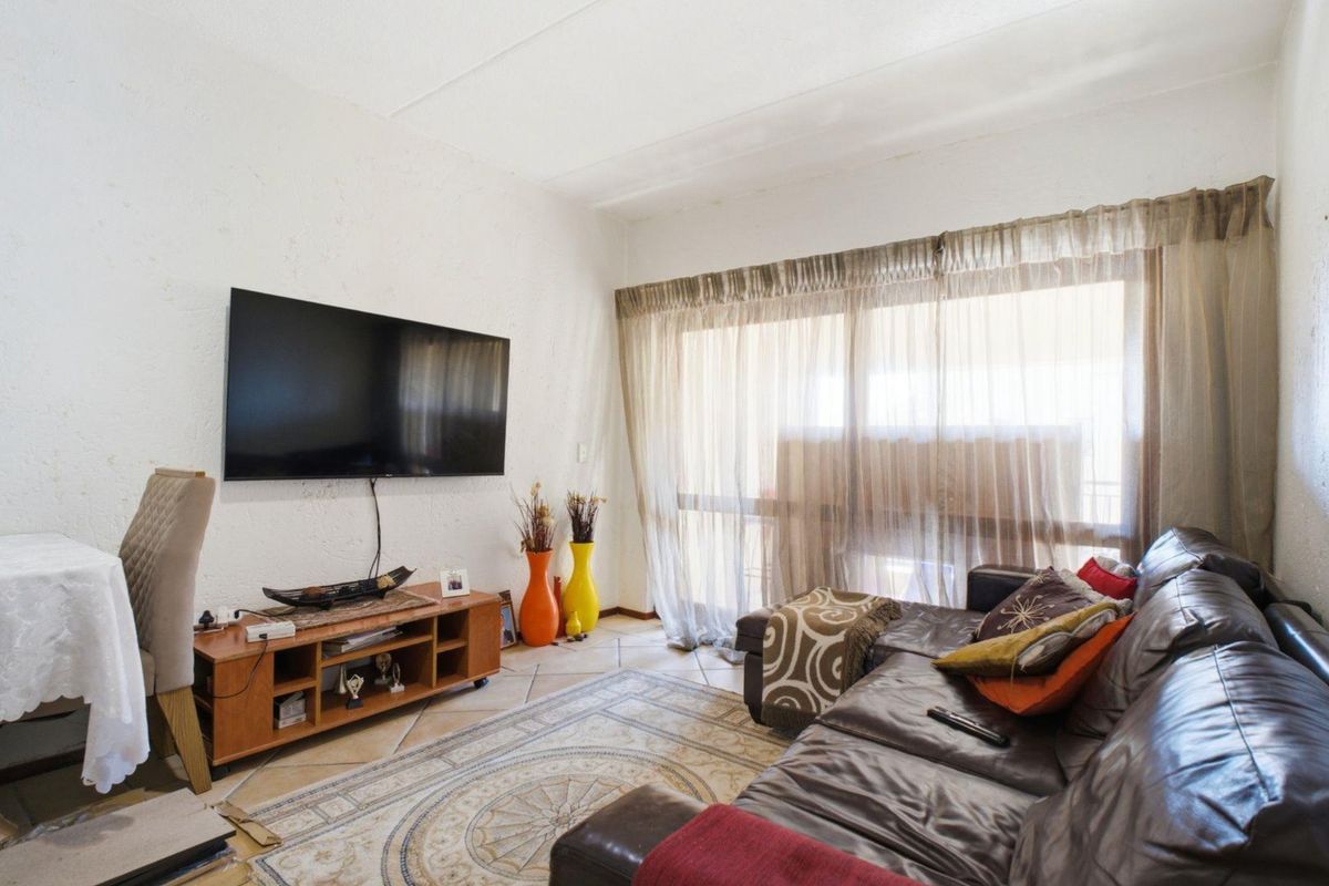 A living room featuring tiled flooring, textured walls, and a large sliding glass door providing natural light.