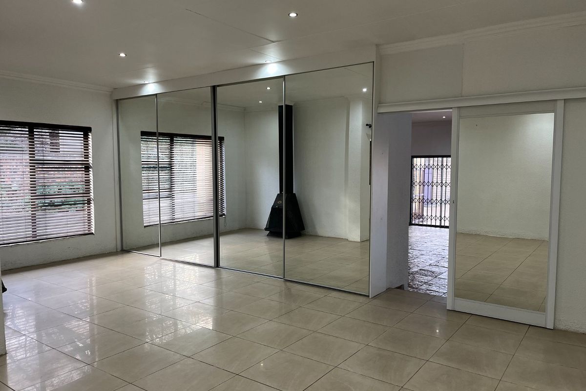 Spacious living area featuring large mirrored built-in cupboards, a modern freestanding fireplace, tiled flooring, and recessed lighting throughout.