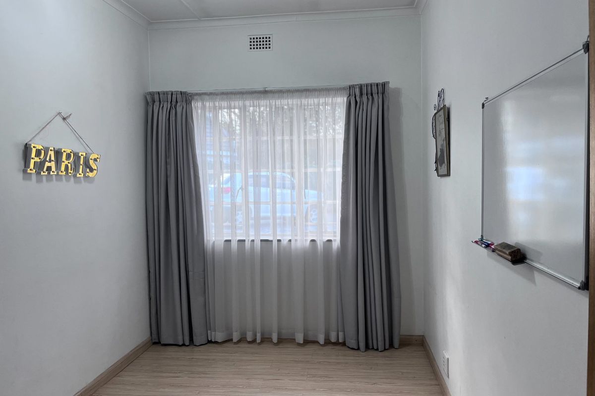 A bright, empty bedroom featuring light-toned laminate flooring, neutral walls, and a window dressed with floor-to-ceiling curtains.