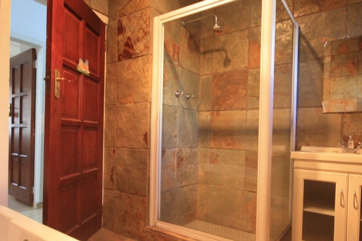 A bathroom featuring a shower enclosure with tiled walls and a vanity cabinet with a basin.