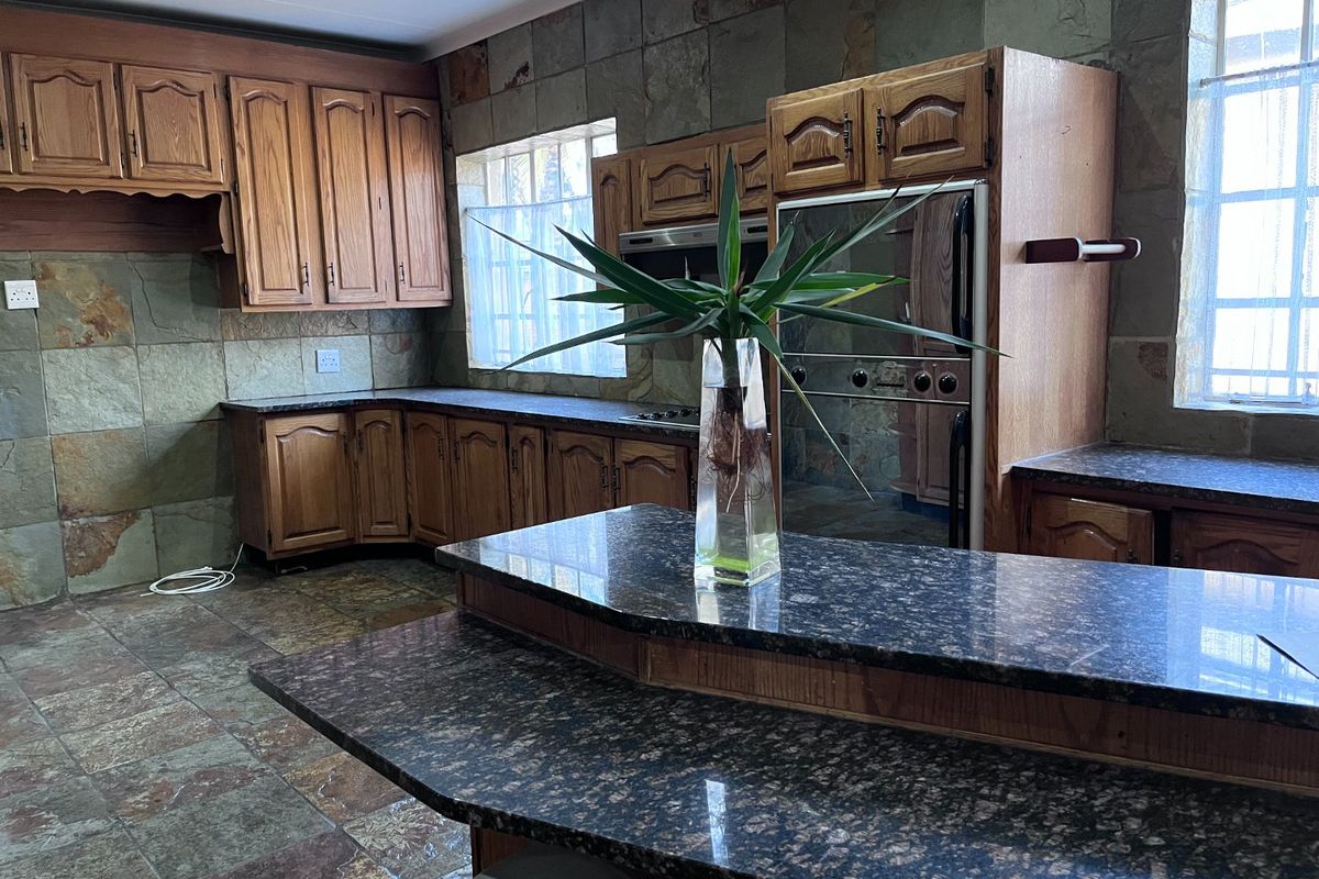 Spacious kitchen featuring extensive wooden cabinetry, granite countertops, a central island, and distinctive stone tile wall and floor finishes.