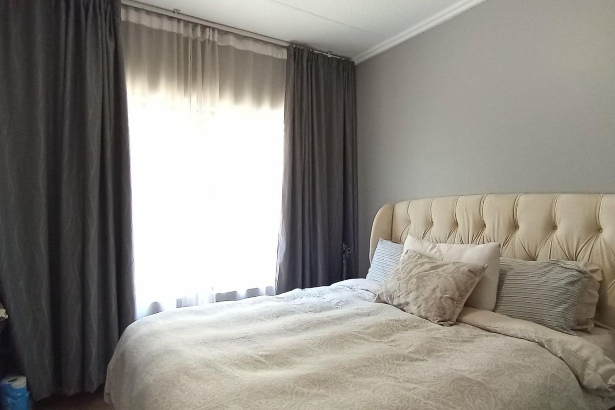 A well-lit bedroom featuring neutral wall tones, coving, and floor-to-ceiling curtains.