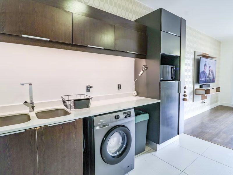 Modern open-plan living area featuring a sleek kitchen with dark cabinetry, stone countertops, integrated appliances, and a wall-mounted media console.