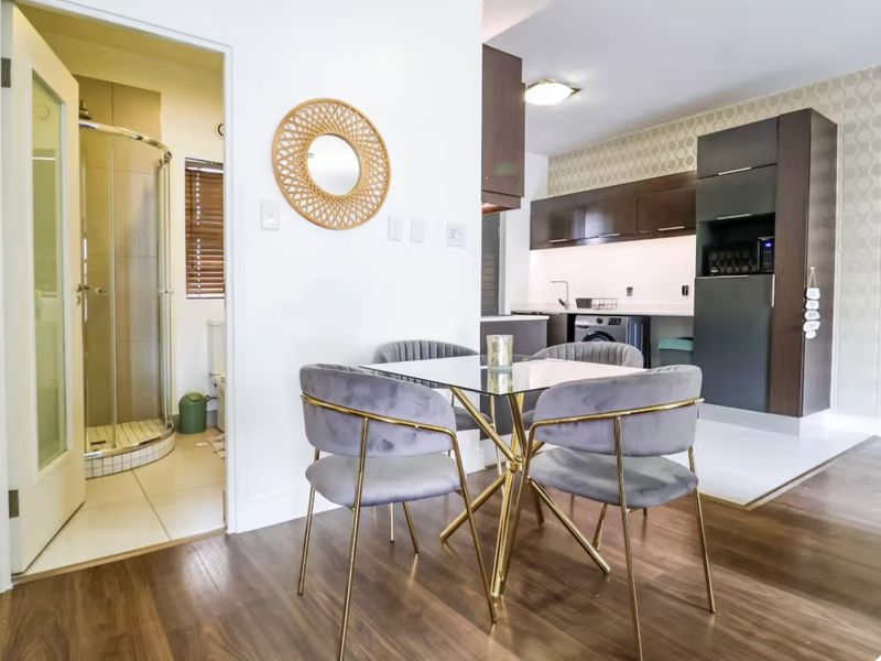 Open-plan living and dining area featuring modern dark cabinetry, laminate flooring, and direct access to a tiled bathroom with a glass shower enclosure.