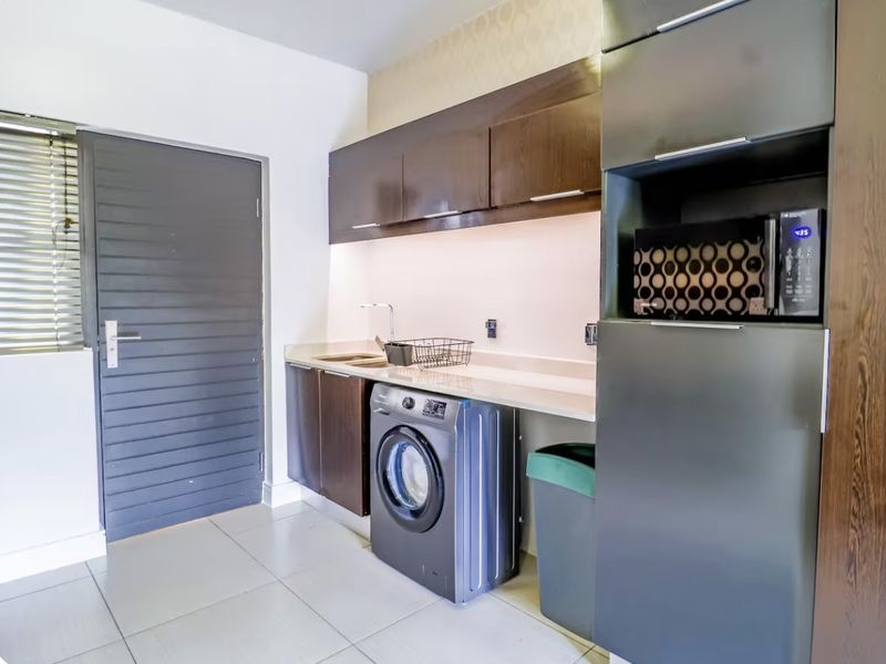 A functional laundry room featuring dark wood cabinetry, stone-look countertops, a stainless steel sink, and dedicated space for a washing machine.