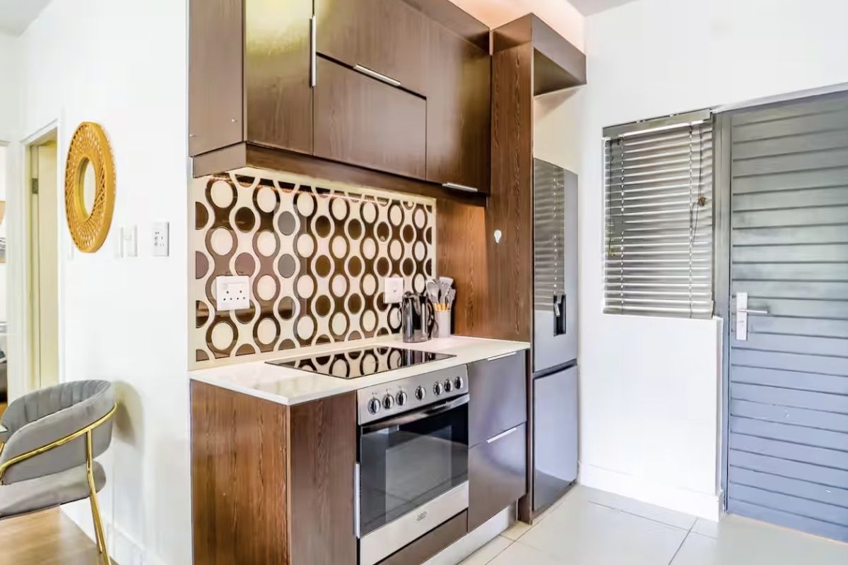 Modern kitchen featuring dark wood cabinetry, integrated electric oven and hob, decorative tiled backsplash, and neutral floor tiles.