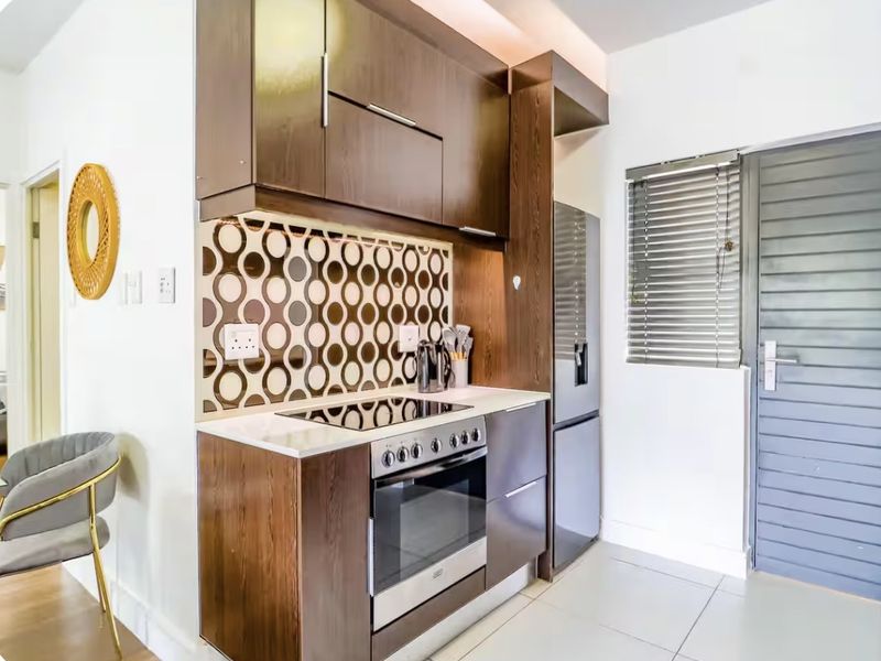 Modern kitchen featuring dark wood cabinetry, integrated electric oven and hob, decorative tiled backsplash, and neutral floor tiles.