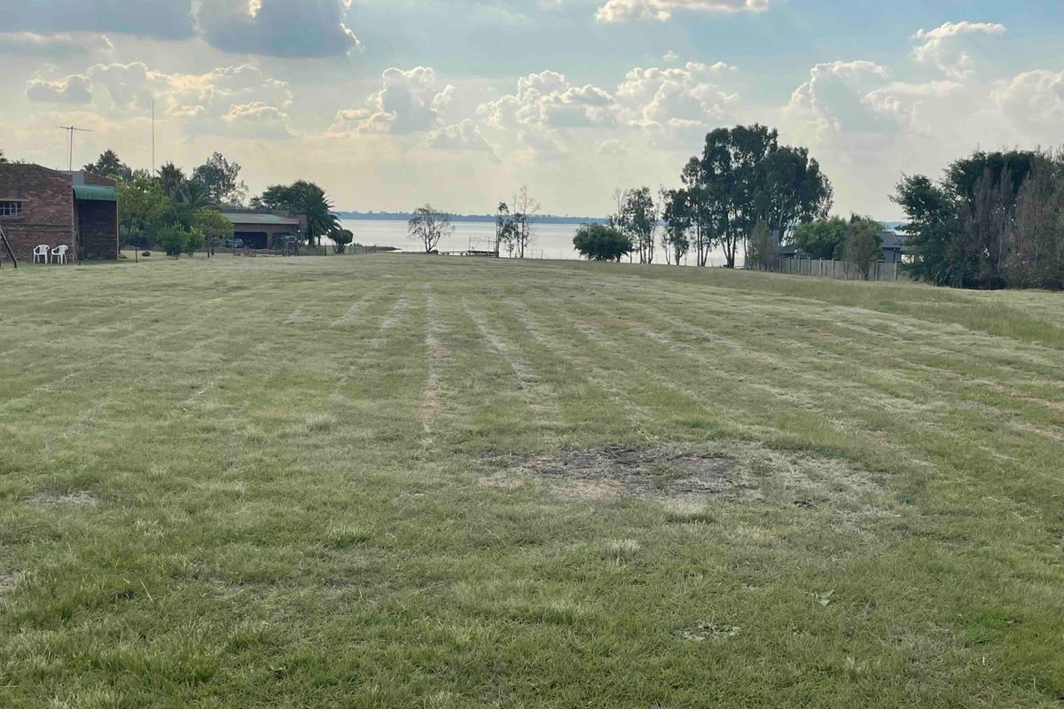 A spacious vacant residential plot featuring expansive grassed areas and scenic waterfront views.