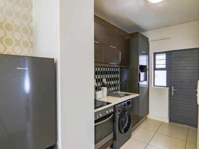 Compact modern kitchen featuring dark cabinetry, patterned backsplash, built-in oven, hob, and integrated laundry appliance with tiled flooring.