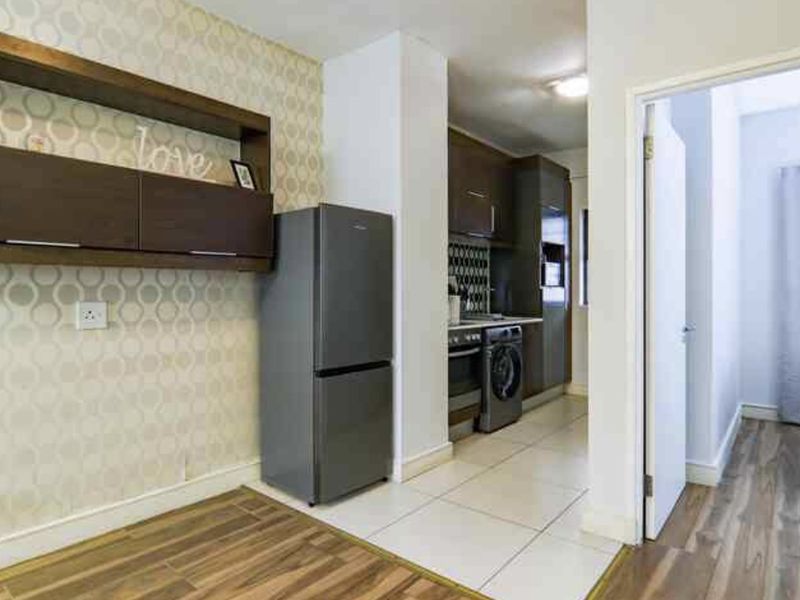 A compact kitchen area featuring tiled and laminate flooring, built-in cabinetry, and decorative wallpaper, leading into an adjacent living or bedroom space.