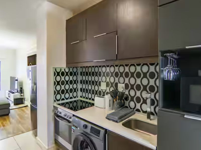 Modern open-plan kitchen featuring dark cabinetry, integrated appliances, and a distinctive patterned backsplash, seamlessly flowing into the adjacent living area.