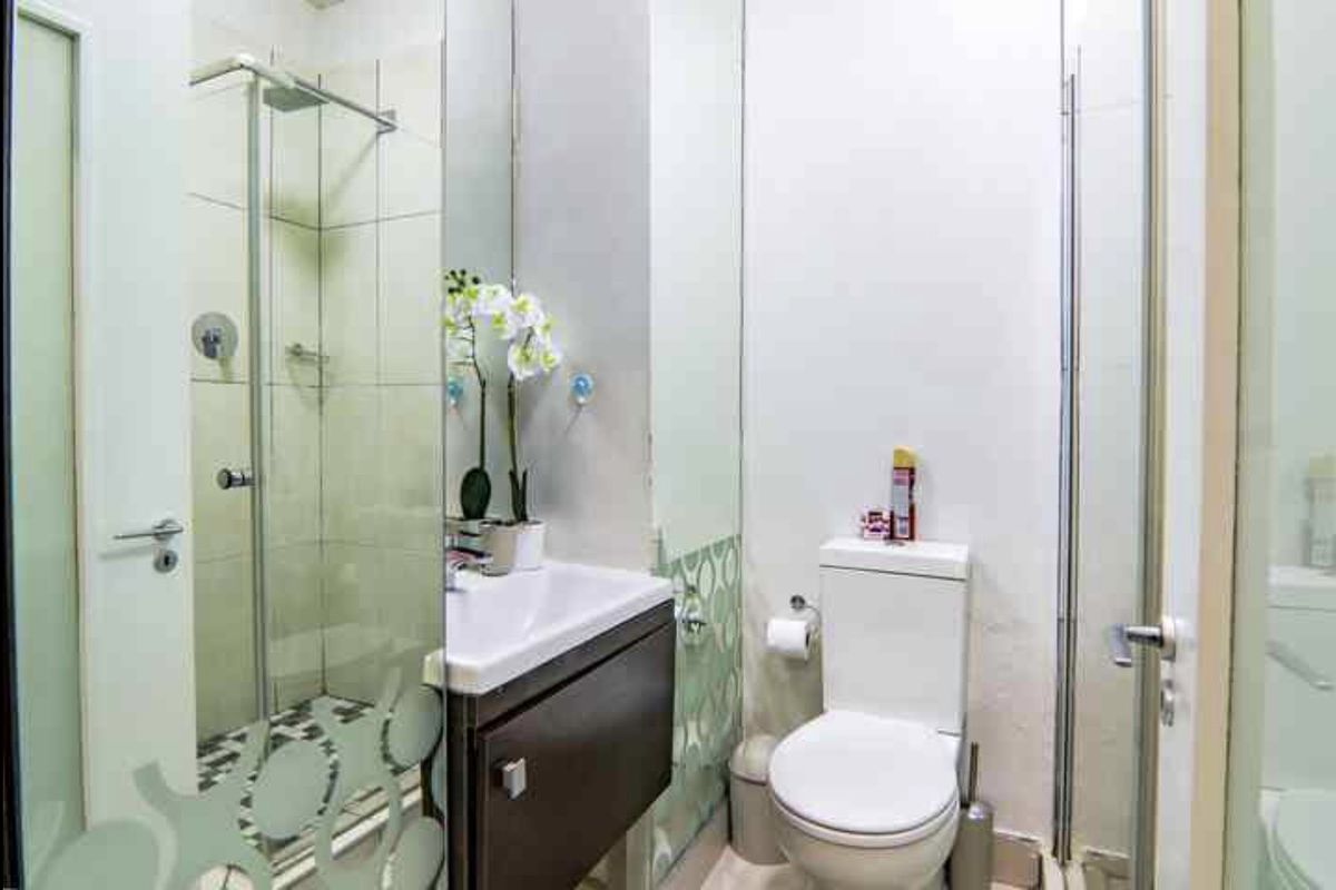 Compact bathroom featuring a glass-enclosed shower, wall-mounted vanity with basin, and a standard toilet with tiled finishes.