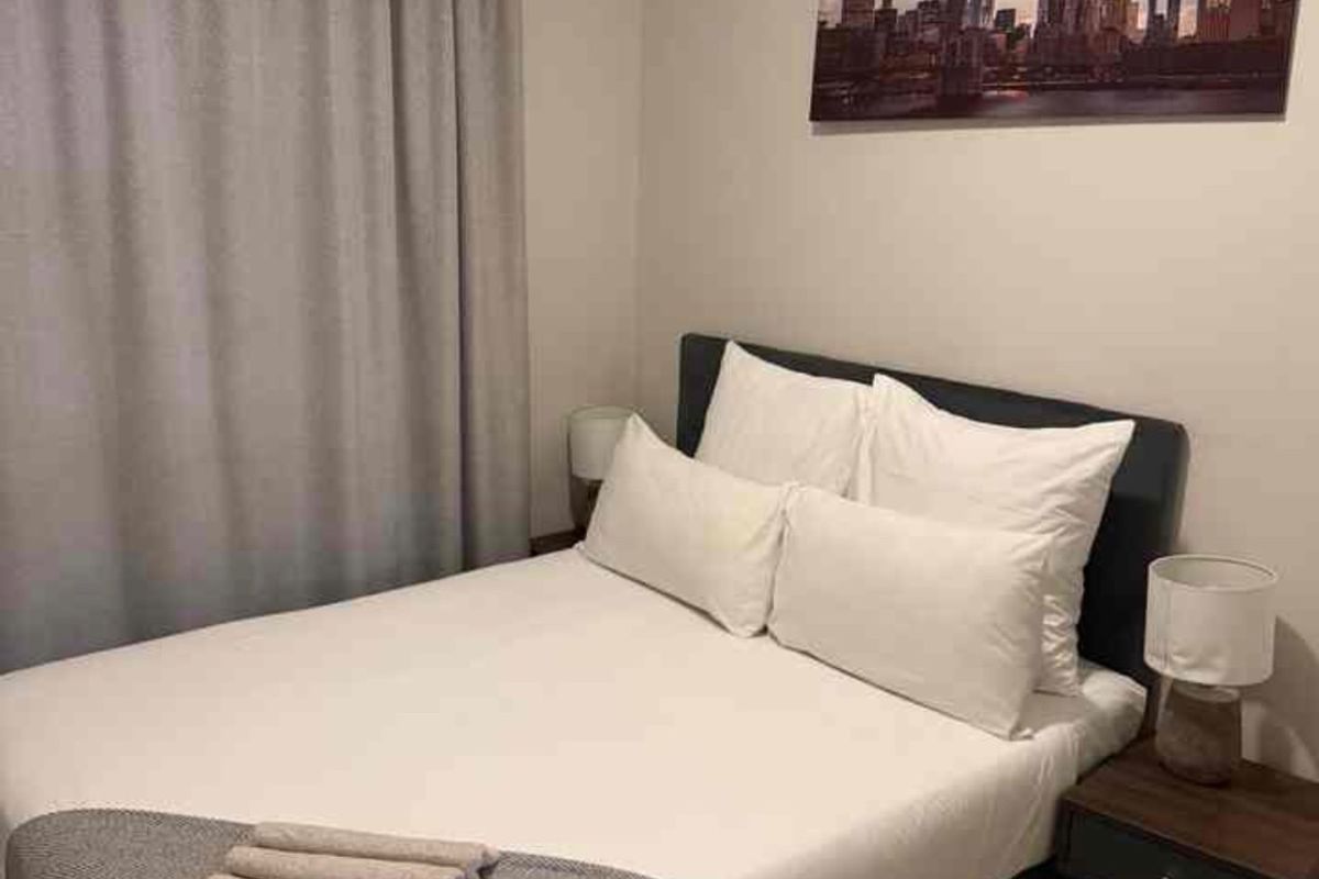 A cozy bedroom featuring neutral wall tones, laminate flooring, and window curtains.
