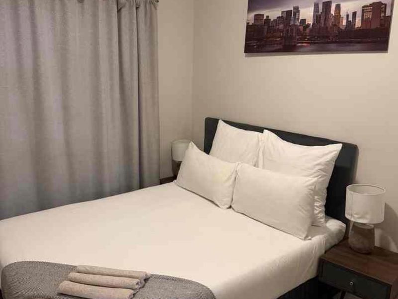 A cozy bedroom featuring neutral wall tones, laminate flooring, and window curtains.