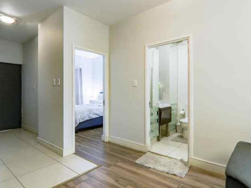 A clean, neutral hallway connecting the living area to the bedroom and bathroom, featuring a mix of tiled and laminate flooring.