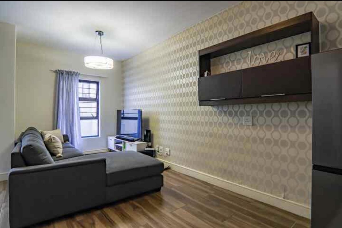 A living room featuring laminate flooring, a patterned feature wall, and built-in wall-mounted cabinetry.