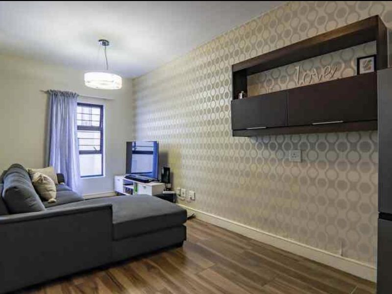 A living room featuring laminate flooring, a patterned feature wall, and built-in wall-mounted cabinetry.