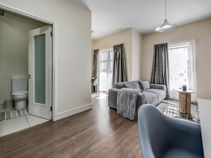 Open plan living area featuring laminate flooring, neutral walls, and direct access to a private bathroom with a modern frosted glass door.