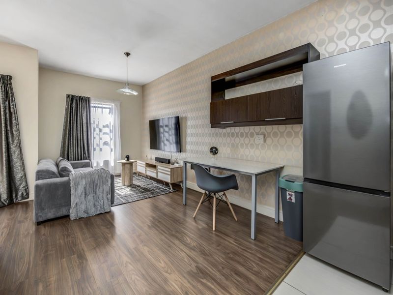 An open-plan living area featuring wood-look laminate flooring, decorative wallpaper, and built-in wall cabinetry, creating a functional and modern living space.