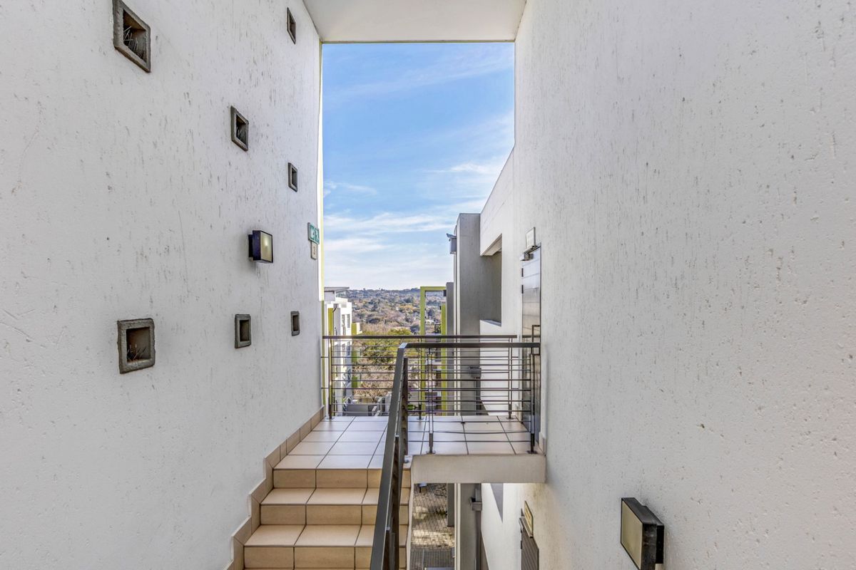 An exterior view of an apartment complex walkway featuring a tiled staircase, metal balustrades, and recessed wall lighting with views of the surrounding area.