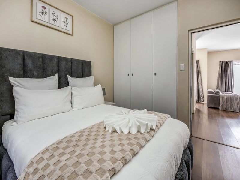 A well-maintained bedroom featuring laminate flooring and a built-in wardrobe, with a view into the adjacent living area.