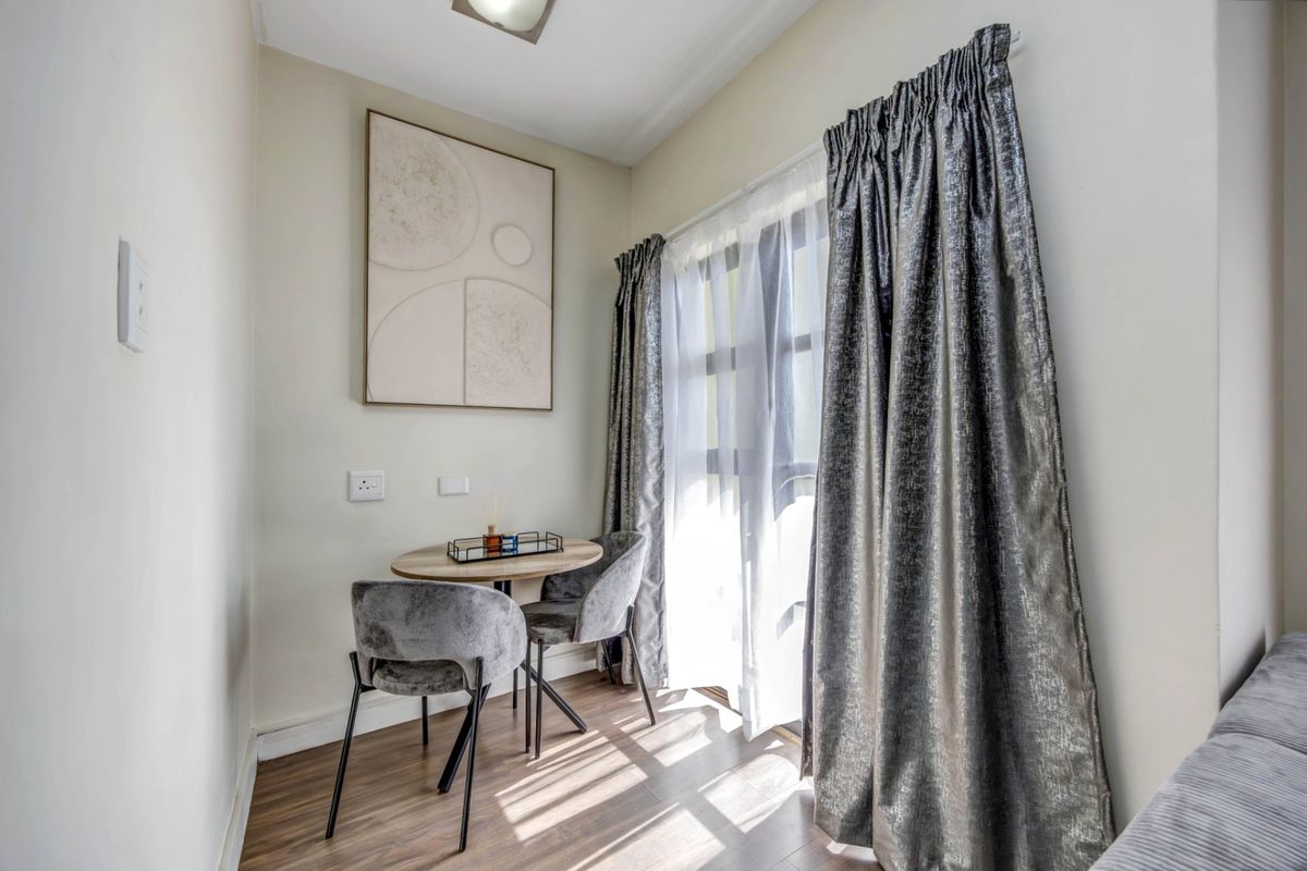 A bright and compact living area featuring laminate flooring and large windows with curtain tracks, offering a cozy space for relaxation.