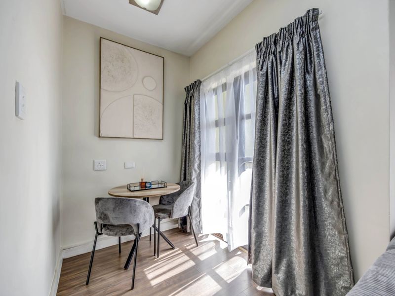 A bright and compact living area featuring laminate flooring and large windows with curtain tracks, offering a cozy space for relaxation.