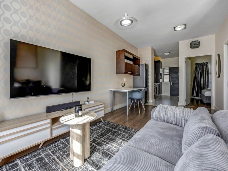 Open-plan living area featuring laminate flooring, modern lighting, and a functional layout connecting to the kitchen and adjacent rooms.