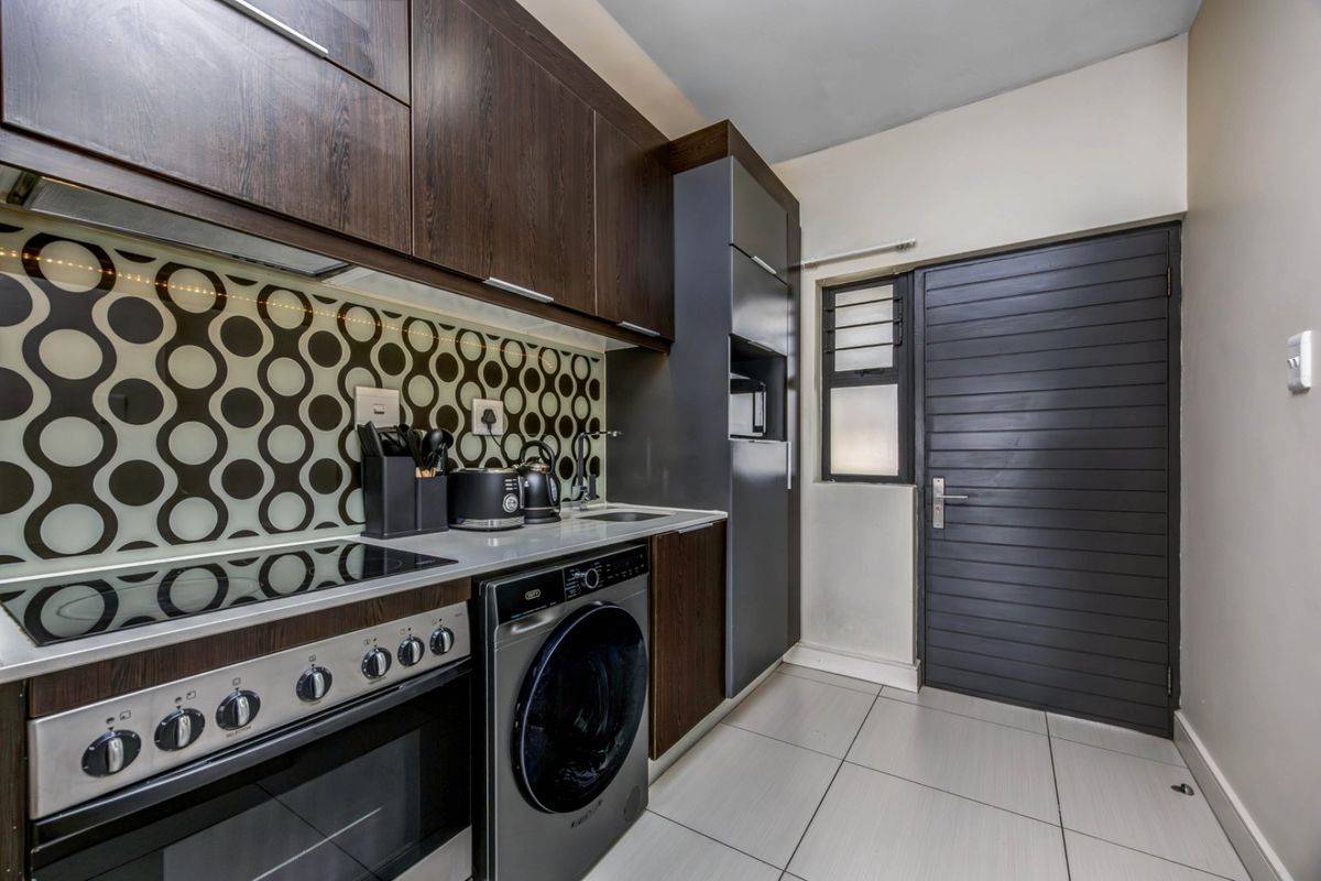 Modern kitchen featuring dark wood cabinetry, patterned backsplash, integrated oven and hob, and tiled flooring with direct access to an exterior door.
