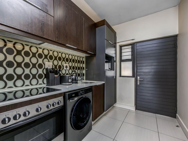 Modern kitchen featuring dark wood cabinetry, patterned backsplash, integrated oven and hob, and tiled flooring with direct access to an exterior door.