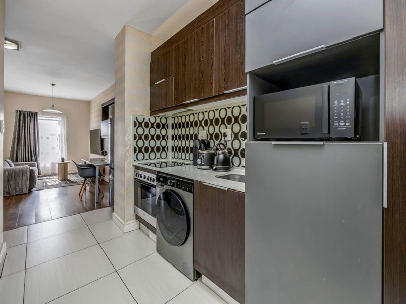 Modern open-plan apartment featuring a compact kitchen with dark wood cabinetry, integrated appliances, and tiled flooring, flowing into a comfortable living area.
