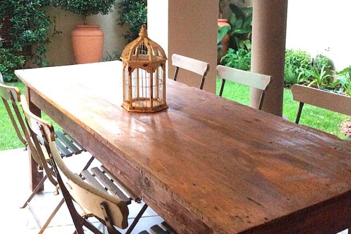 A covered outdoor patio area featuring tiled flooring and structural columns, overlooking a landscaped garden space.