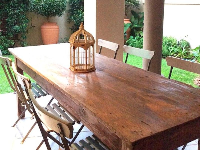A covered outdoor patio area featuring tiled flooring and structural columns, overlooking a landscaped garden space.