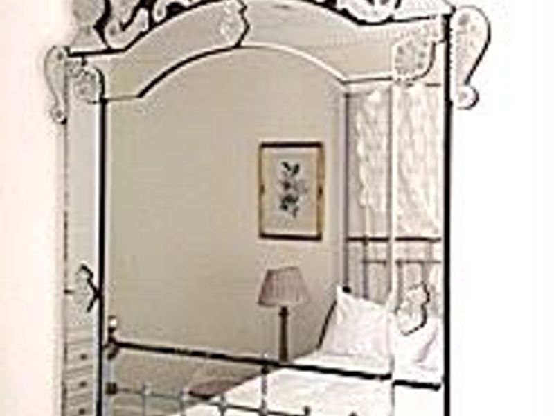 A decorative wall mirror reflecting a bedroom interior.